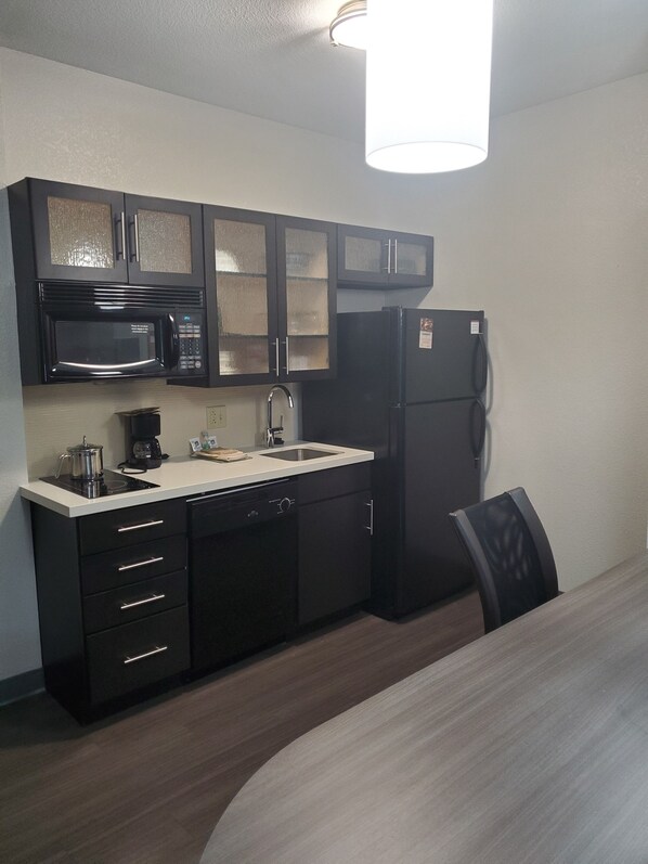 A compact kitchen with dark cabinetry, a microwave, a refrigerator, and a sink.