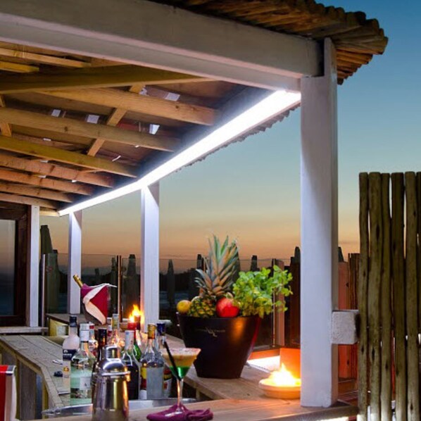 A covered outdoor area with a wooden ceiling, a table with drinks and a fruit bowl, and a lit candle. - Conchiglia Azzurra Resort & Beach (Porto Cesareo)