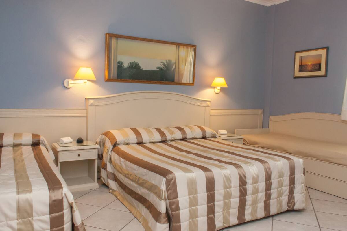 Habitación de hotel con dos camas, un sofá y dos lámparas de noche.