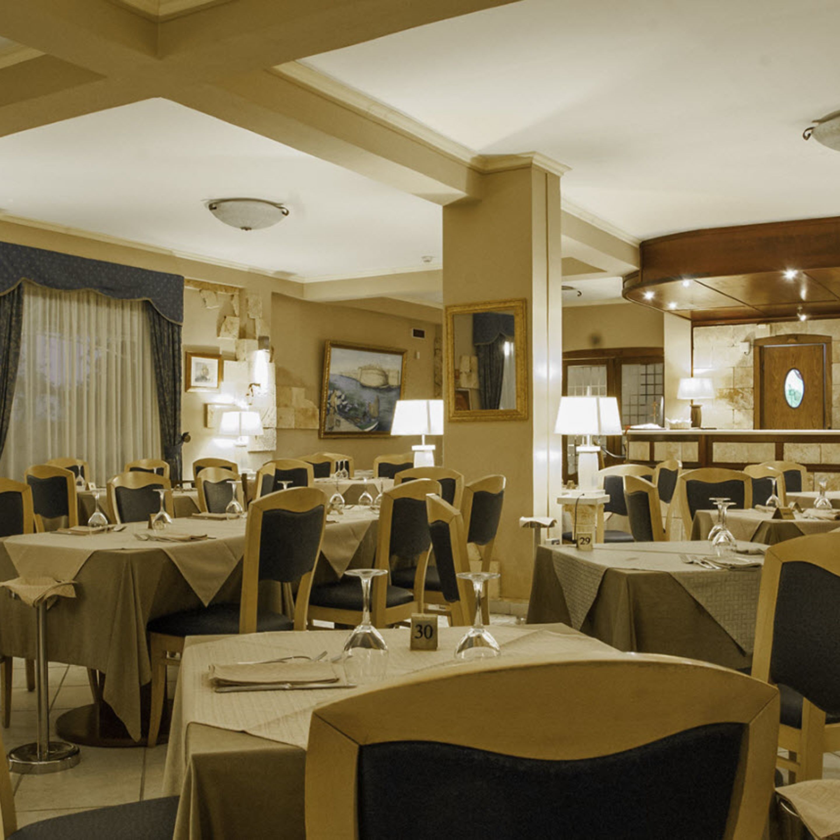 A hotel dining room with multiple tables and chairs, each set with tableware and a number on the table.