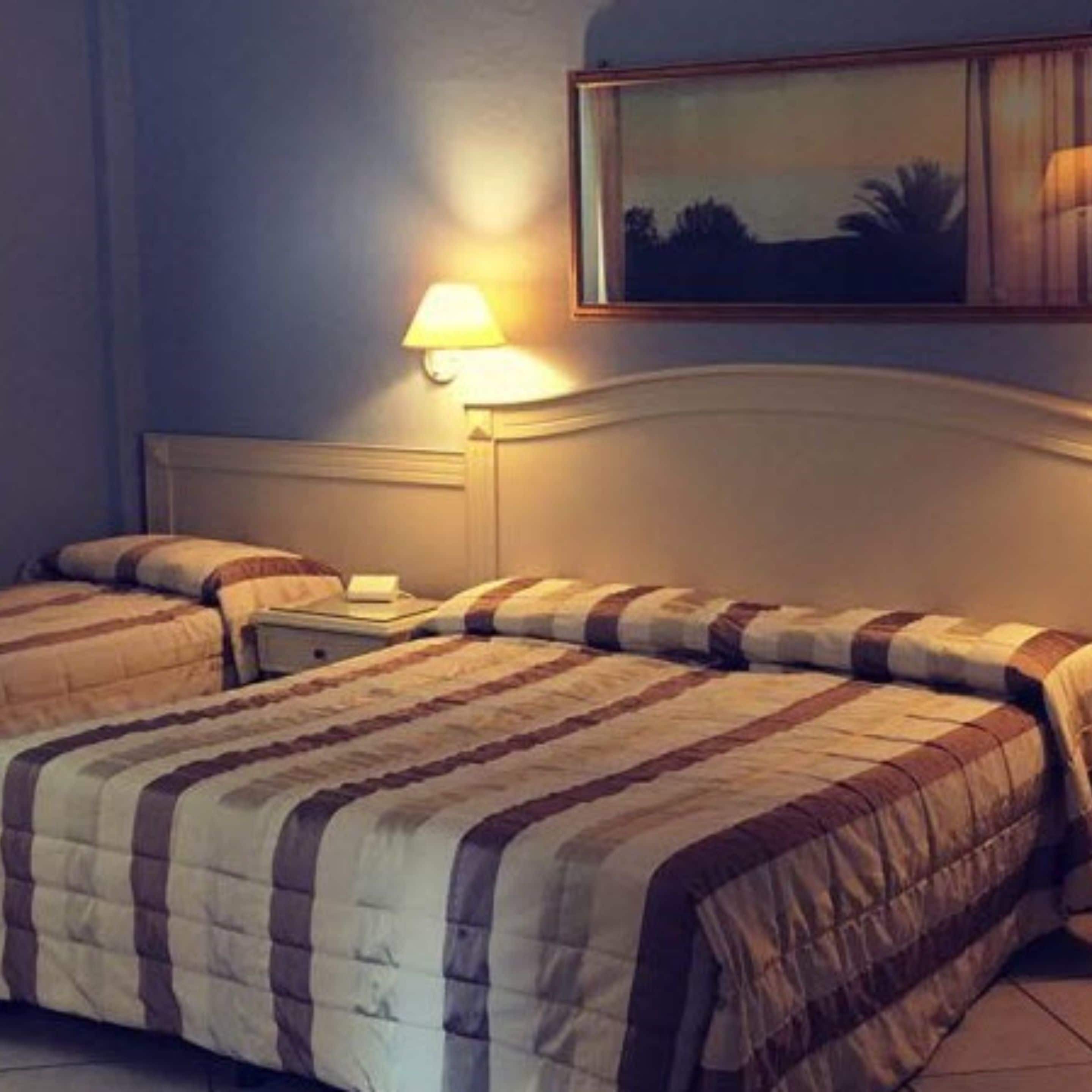 A hotel room with a double bed, a nightstand, a lamp, and a painting on the wall.