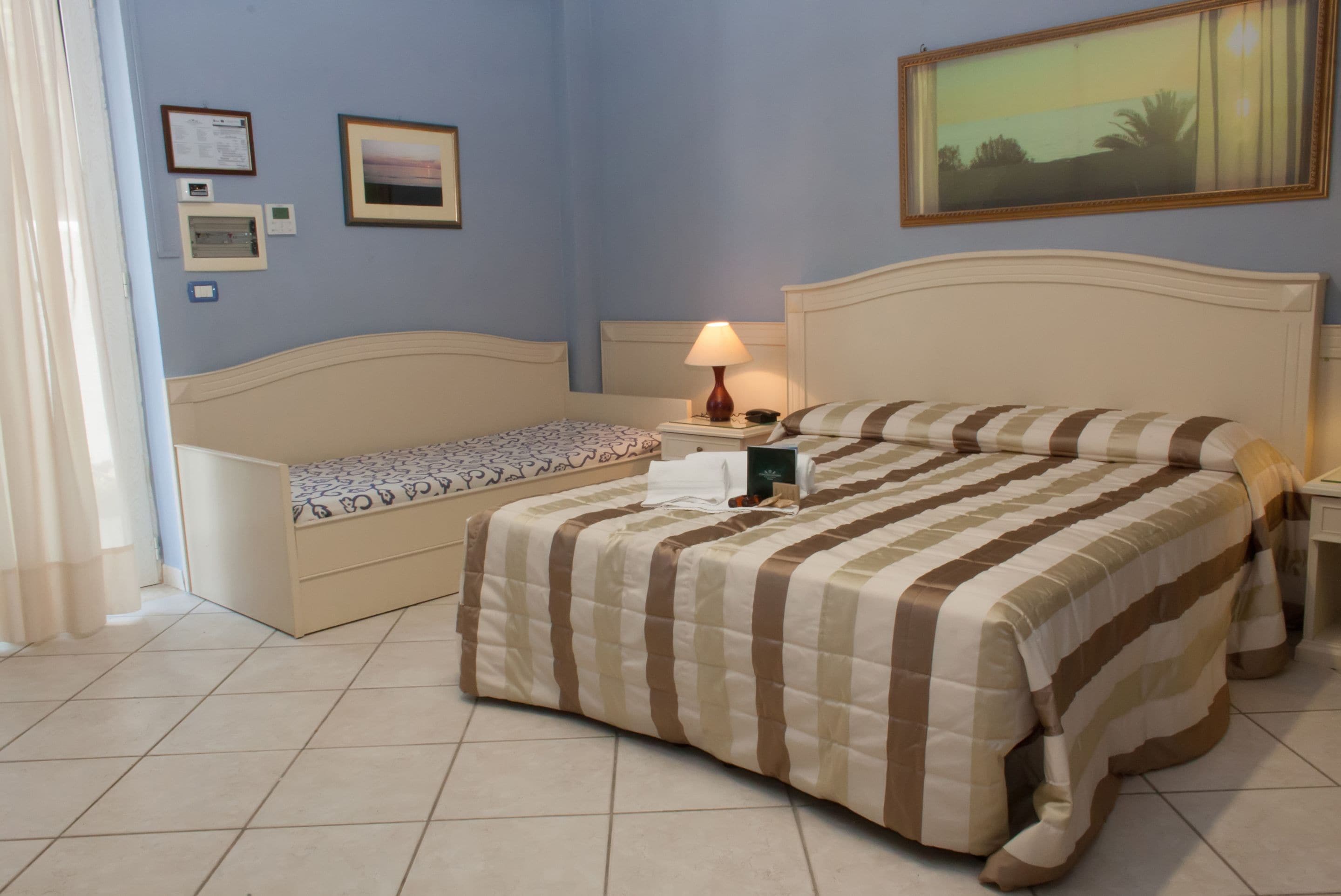 A hotel room with a bed, a bedside table with a lamp, a small bedside table with a phone, and a wall-mounted picture.