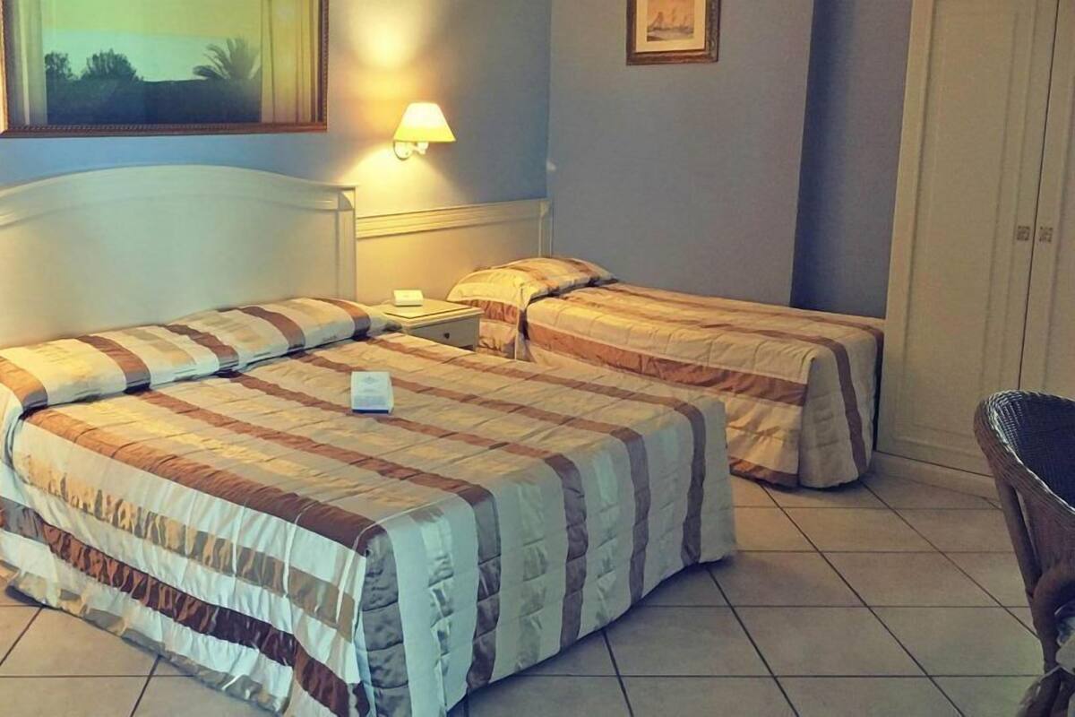 Una habitación de hotel con dos camas, una mesita de noche, una silla y un cuadro en la pared.