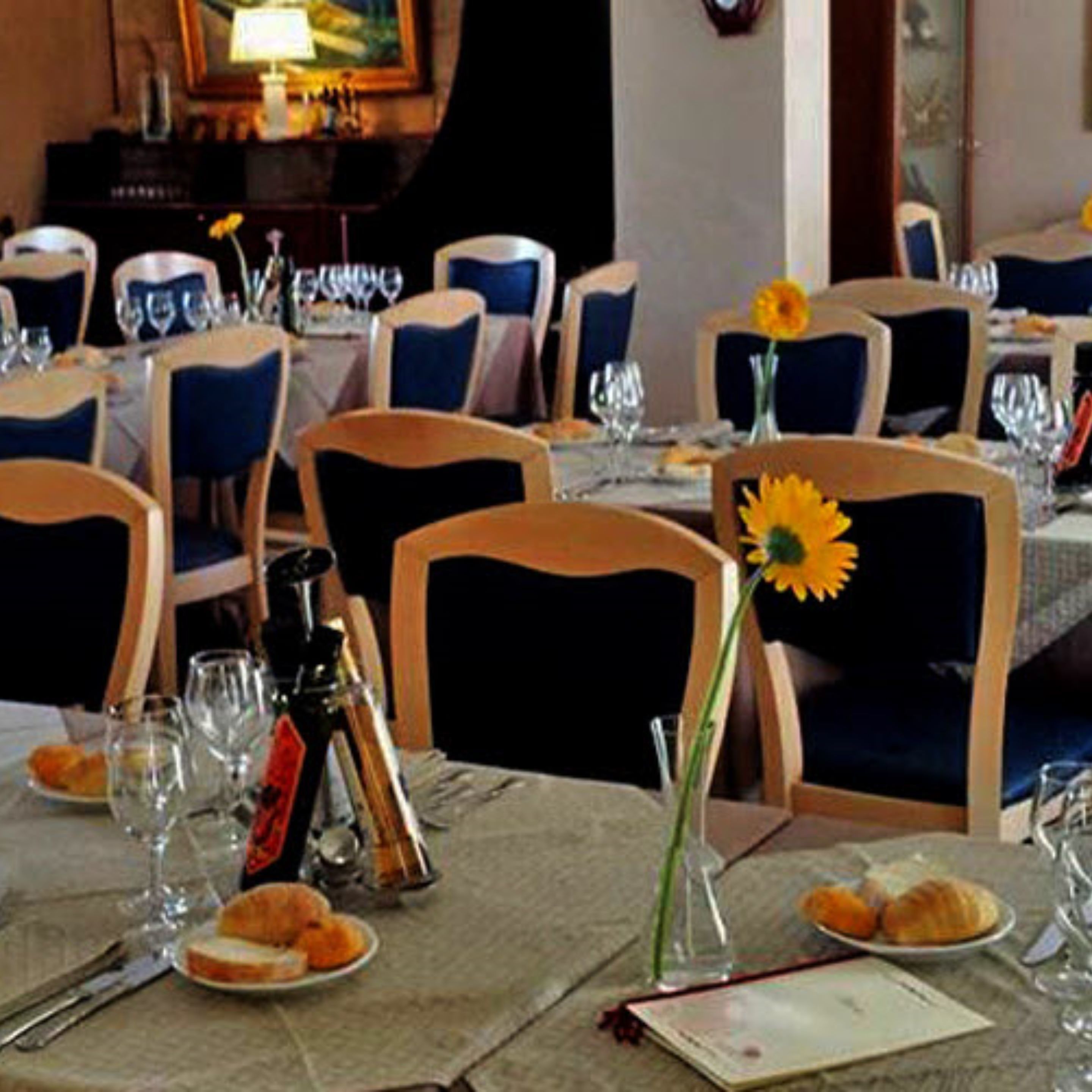 A dining area with tables set for two, each with a vase of sunflowers, wine glasses, and plates of food.