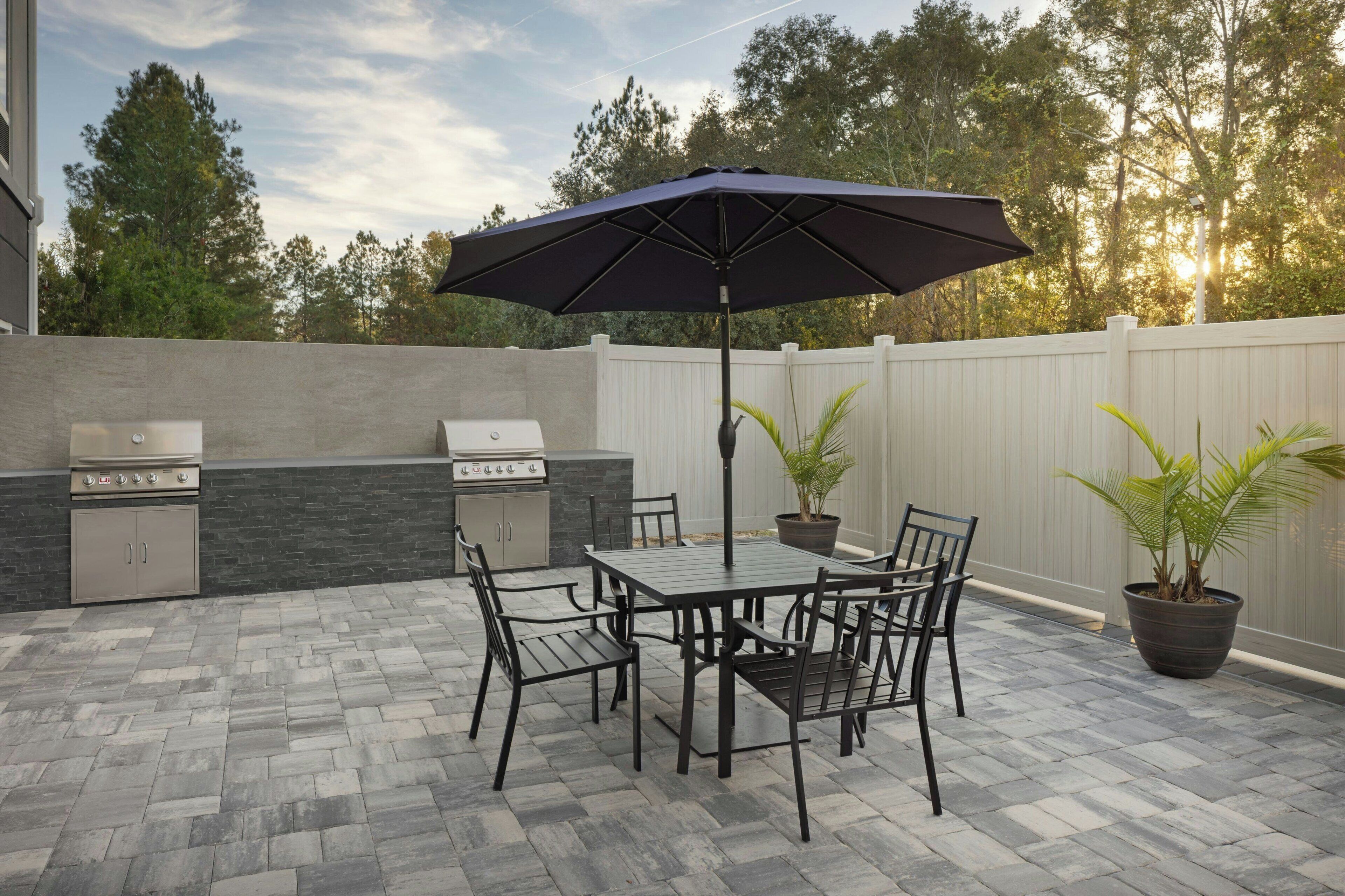 Une terrasse extérieure équipée d’un barbecue, d’une table, de chaises et de plantes en pot.