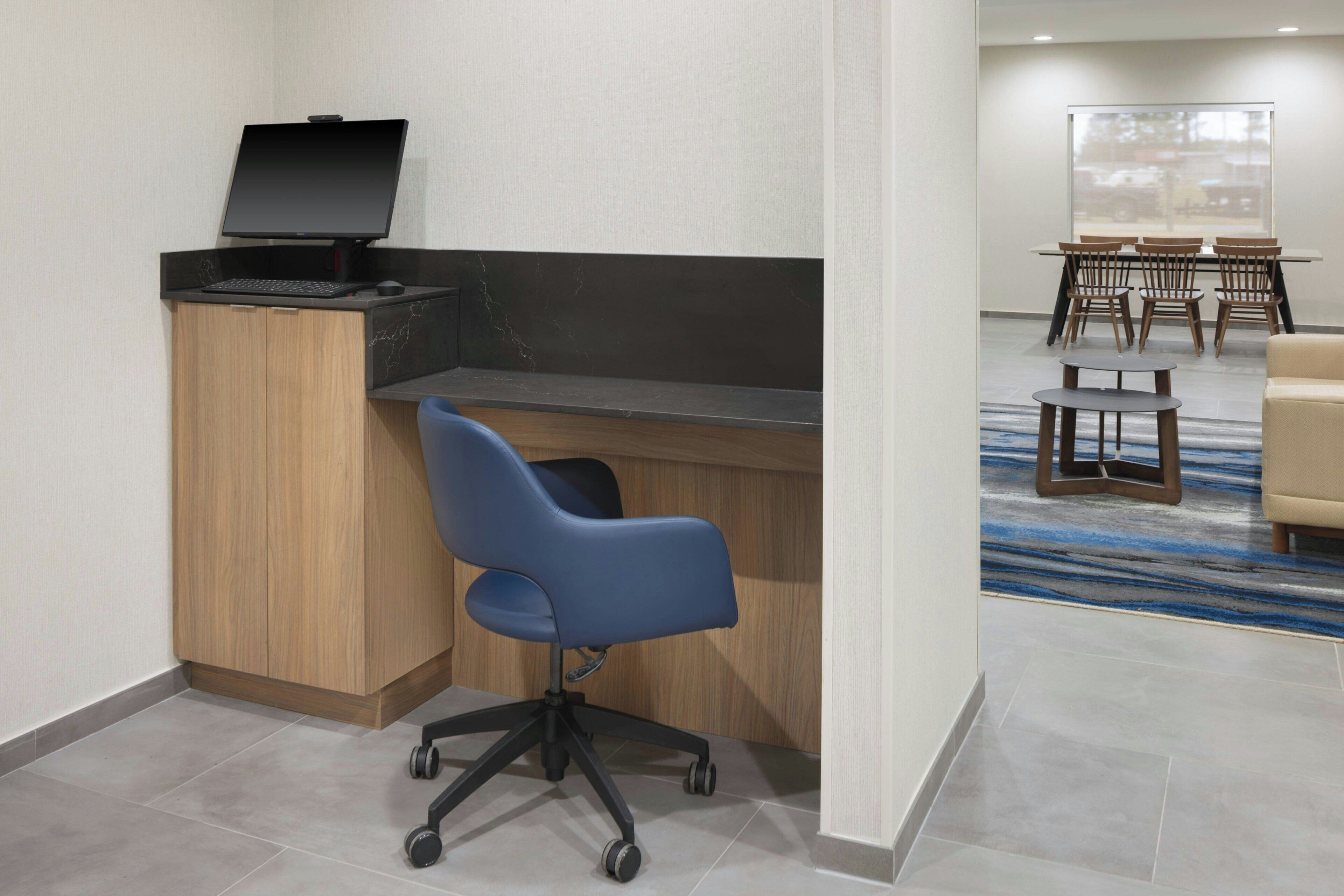 Un espacio de oficina moderno con un escritorio, computadora y una silla de oficina azul. En el fondo, hay una mesa de conferencias con sillas.