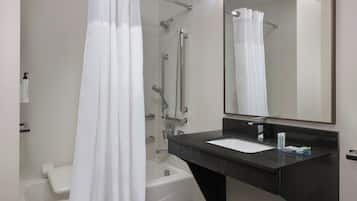 A modern bathroom with a bathtub, a shower with a glass door, a dark marble sink, and a mirror above the sink.