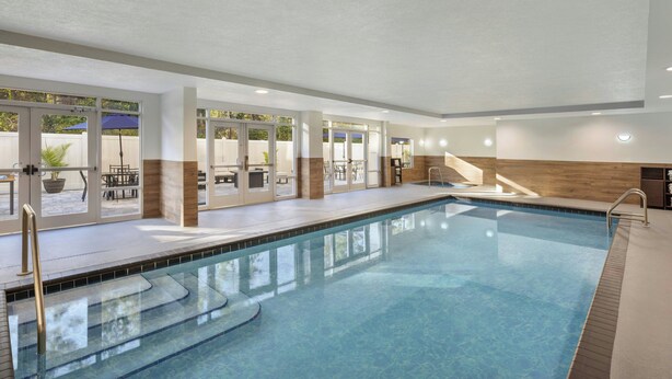 An indoor swimming pool with clear water, surrounded by glass doors and windows, and a wooden deck area. - Fairfield Inn & Suites Lake City (Lake City)