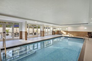Una piscina interior con agua cristalina, rodeada de puertas y ventanas de vidrio, y un área de terraza de madera.