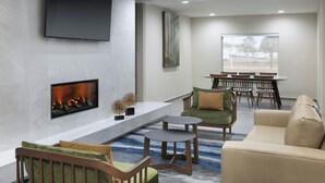 A modern lounge area with a fireplace, comfortable seating, a dining table, and a large window offering a view. - Fairfield Inn & Suites Lake City (Lake City)
