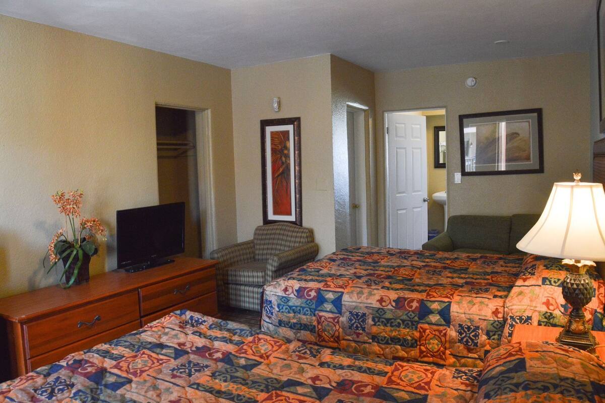 Habitación de hotel con dos camas, televisor, cómoda, silla y lámpara.
