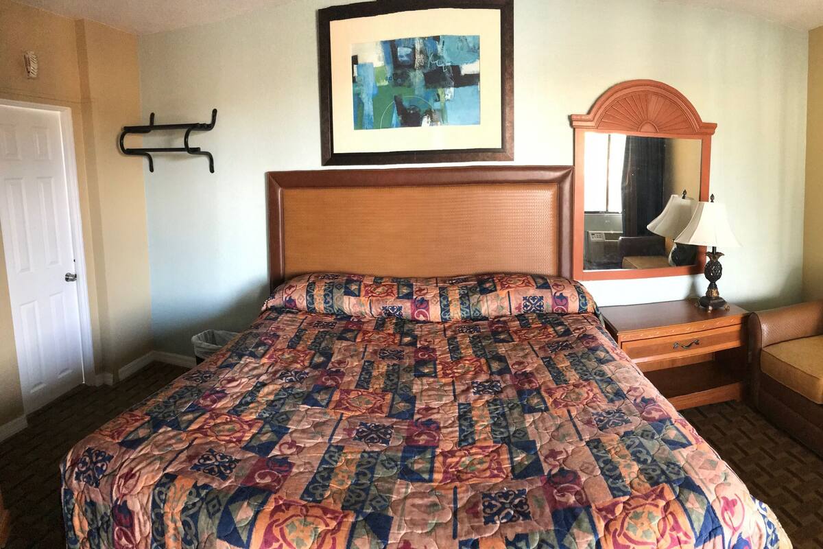 Habitación de hotel con una cama grande, una mesita de noche de madera, un sofá, un espejo y un cuadro en la pared.