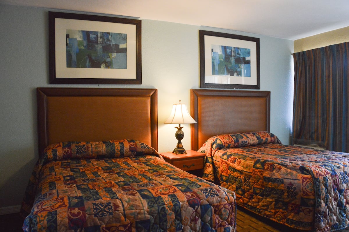 Habitación de hotel con dos camas, cada una con una colcha estampada, una mesita de noche con lámpara y obras de arte enmarcadas en las paredes.