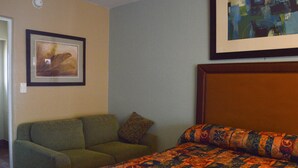 A hotel room with a bed, a green armchair, and two framed artworks on the walls. - San Marina Motel (Daytona Beach)