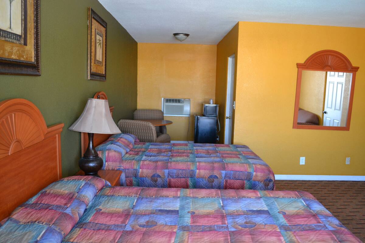 Habitación de hotel con dos camas, televisión, lámpara y espejo en la pared.