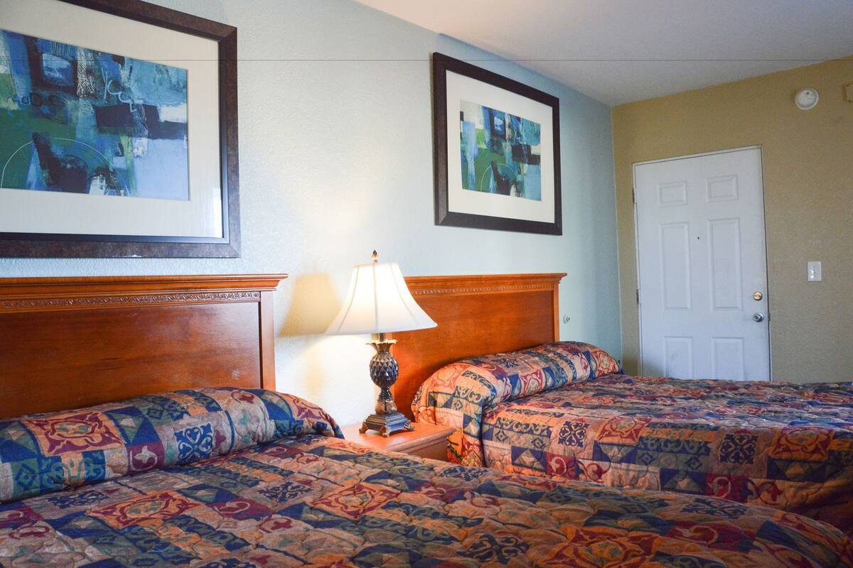 Habitación de hotel con dos camas, una mesita de noche con lámpara y dos cuadros abstractos enmarcados en la pared.