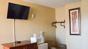 A hotel room with a flat-screen TV mounted on the wall, a wooden dresser, a microwave, a plaid chair, and a framed picture on the wall. - San Marina Motel (Daytona Beach)