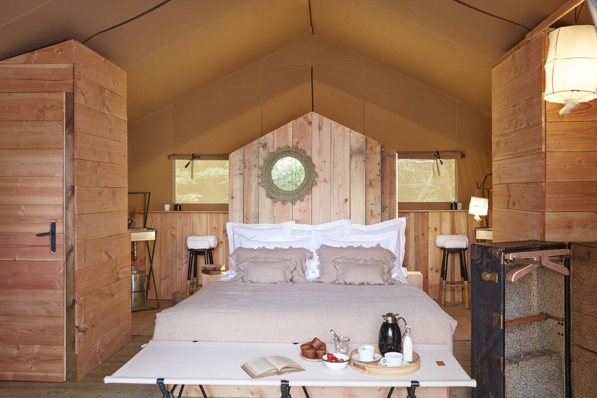 Un dormitorio estilo tienda de madera con una cama, mesitas de noche y una zona para el desayuno.