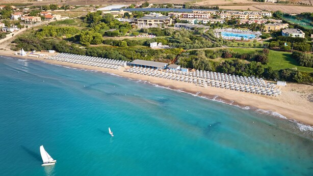 An aerial view of a coastal area with a beach, a marina, and a resort complex. - Serenusa Resort (Licata)