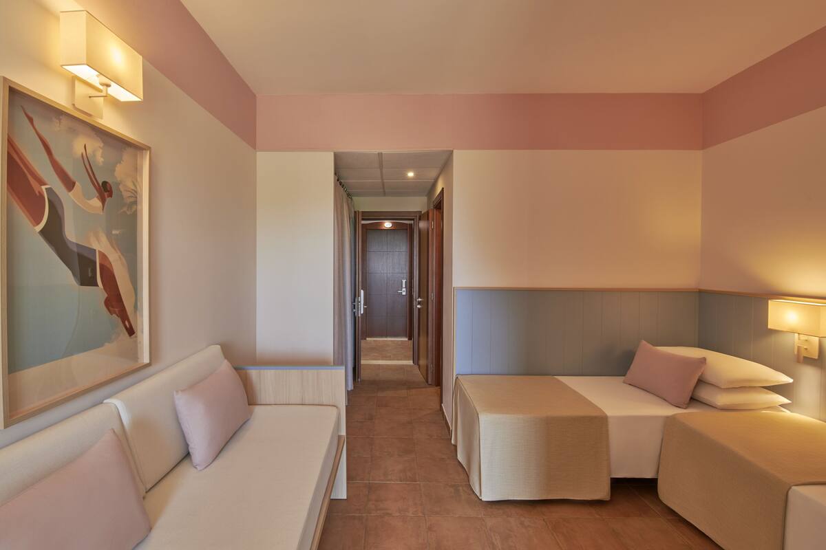A hotel room with a sofa, a bed, a small table, and a painting on the wall.