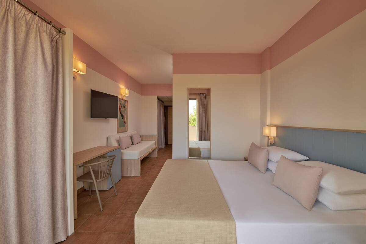 A hotel room with a bed, a desk, a chair, a TV, and a window.