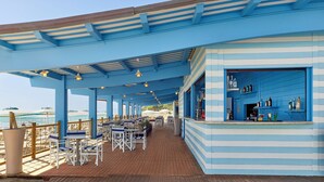 A covered outdoor seating area with tables and chairs, a bar with bottles, and a view of the ocean. - Serenusa Resort (Licata)