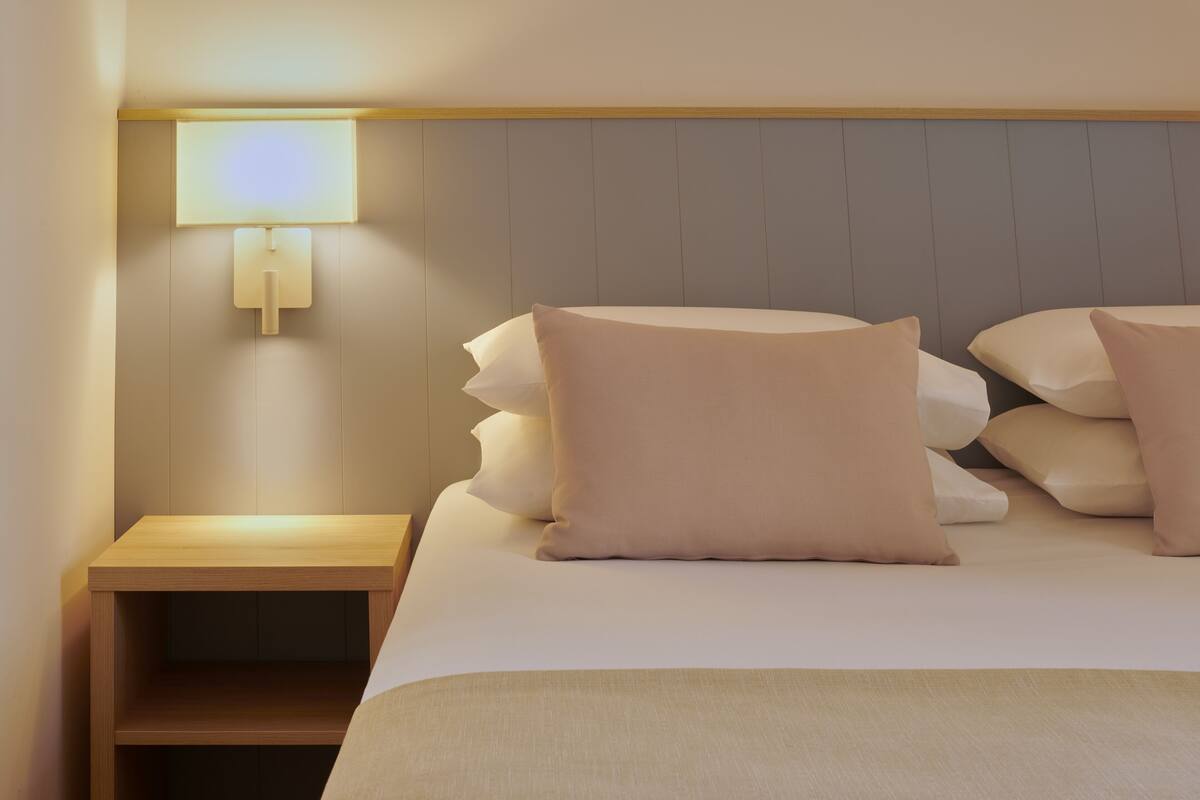 A neatly made bed with multiple pillows and a bedside table with a lamp.