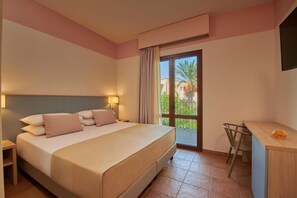 A hotel room with a bed, bedside tables, a desk, and a view of the outdoors. - Serenusa Resort (Licata)