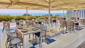 A seaside restaurant with outdoor seating, tables, and chairs, overlooking the ocean. - Serenusa Resort (Licata)