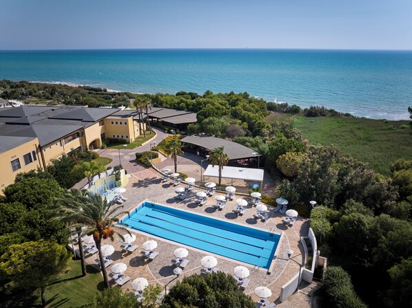 An aerial view of a resort with a swimming pool, lounge chairs, and a view of the sea. - Serenusa Resort (Licata)