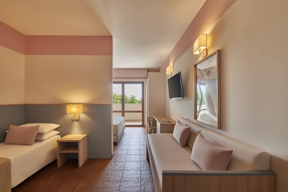 A modern hotel room with a bed, a sofa, a small table, and a TV mounted on the wall.
