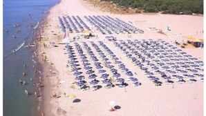A beach with rows of umbrellas and sun loungers, a sandy shore, and a few people in the water.