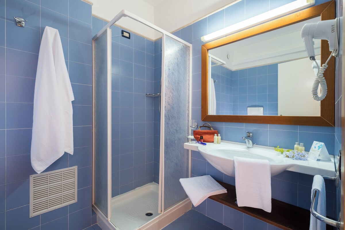 Un baño moderno con azulejos azules, una cabina de ducha de vidrio, un lavamanos con artículos de tocador y un espejo grande.