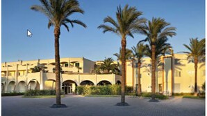 A hotel courtyard with palm trees and a building with arches.
