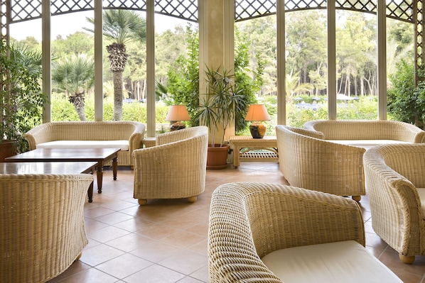 A covered outdoor seating area with wicker furniture and a view of the garden.