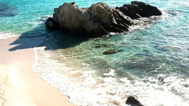 A beach with clear turquoise water and a rocky outcrop. - Hotel Na Forana (Capdepera)