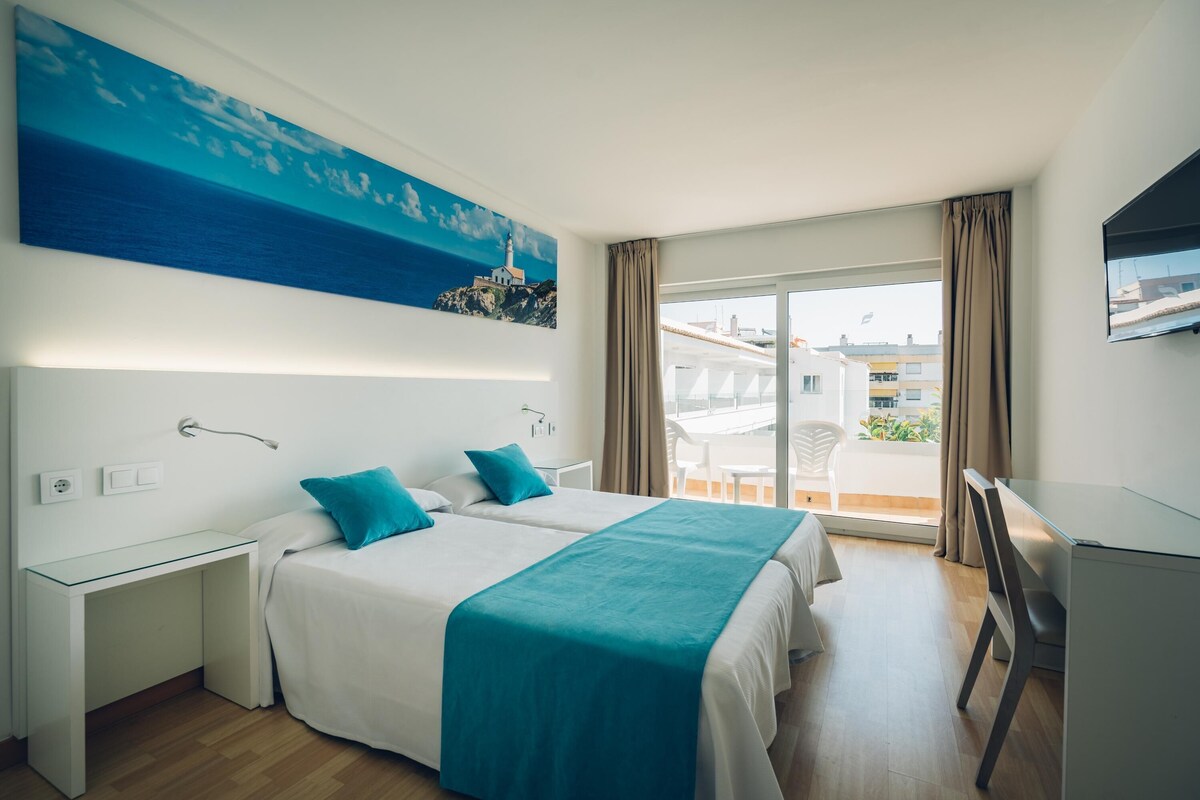 A hotel room with a bed, a desk, and a balcony with a view of buildings.