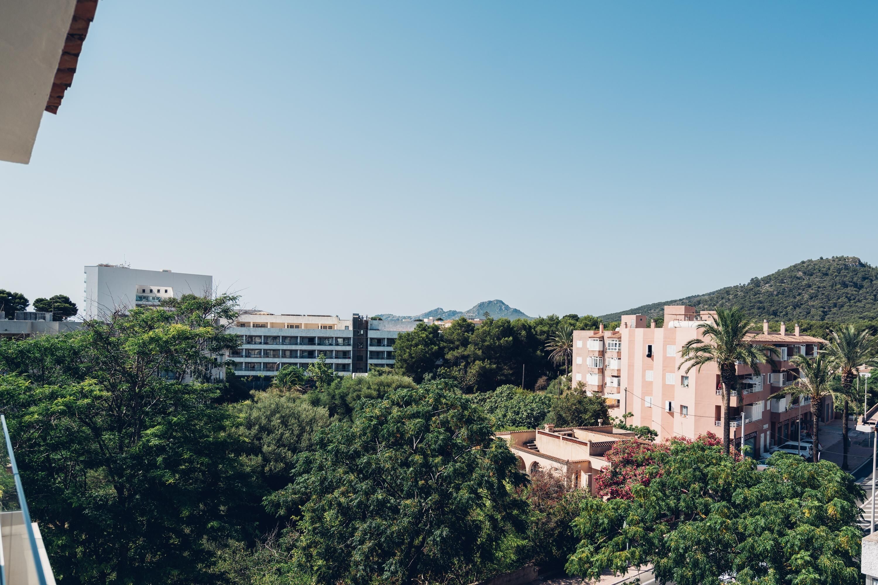 A view of a residential area with buildings, trees, and a hill in the background.