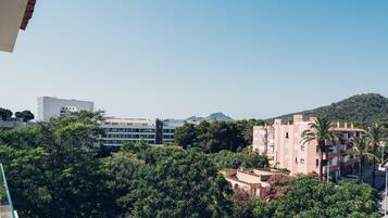 A view of a residential area with buildings, trees, and a hill in the background.