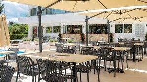 An outdoor seating area with tables and chairs under large umbrellas, a pool, and a bar area. - Hotel THB Dos Playas - Adults Only (Capdepera)