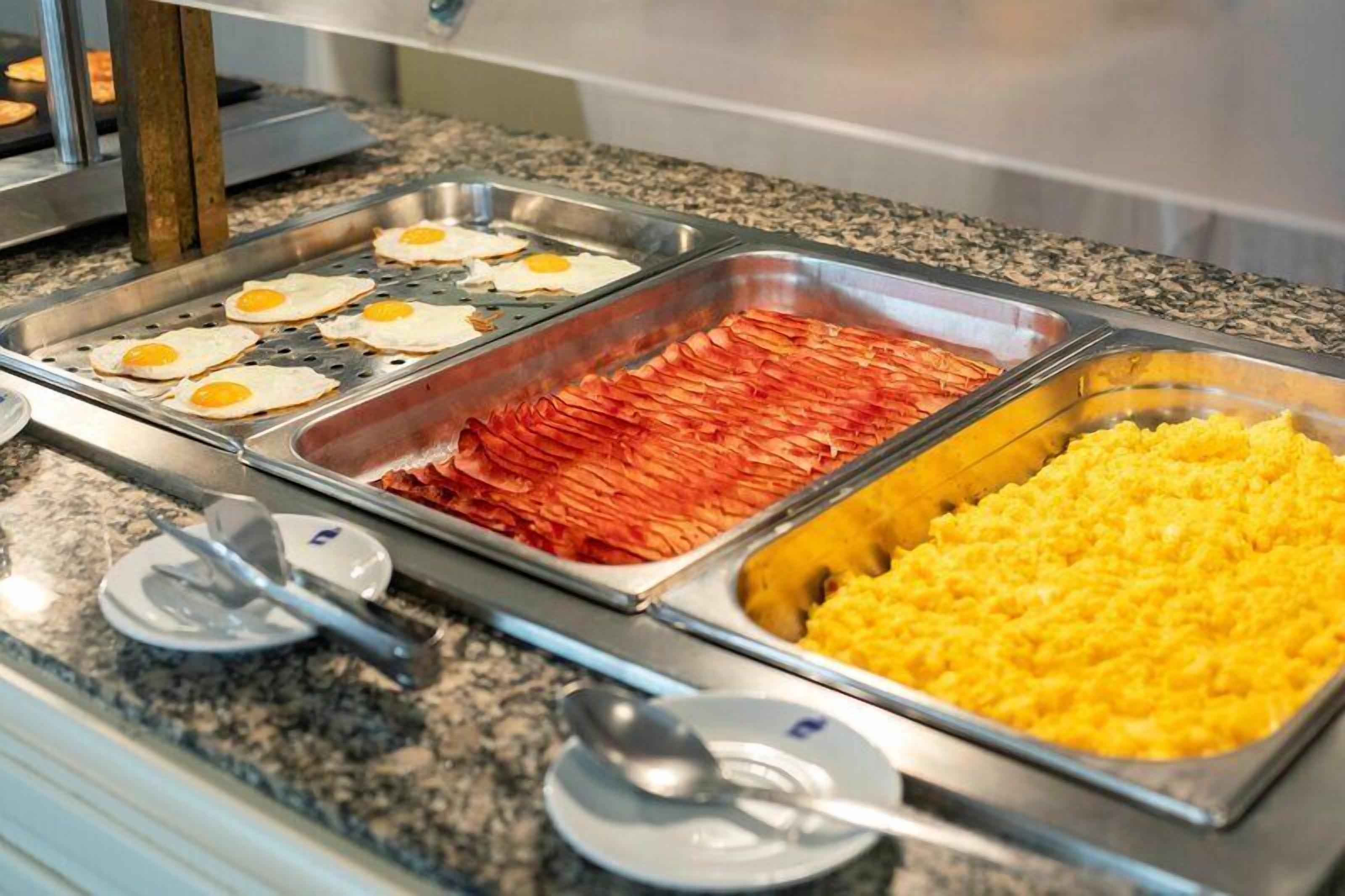 Een ontbijtbuffet met diverse keuze, waaronder eieren, spek en ontbijlgranen.