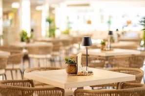 En matplats med flätade stolar och bord, en liten växt på ett bord och en svart lampa.
