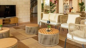 A modern living room with a TV, round wooden tables, white sofas, and a patterned carpet. - Hotel THB Dos Playas - Adults Only (Capdepera)