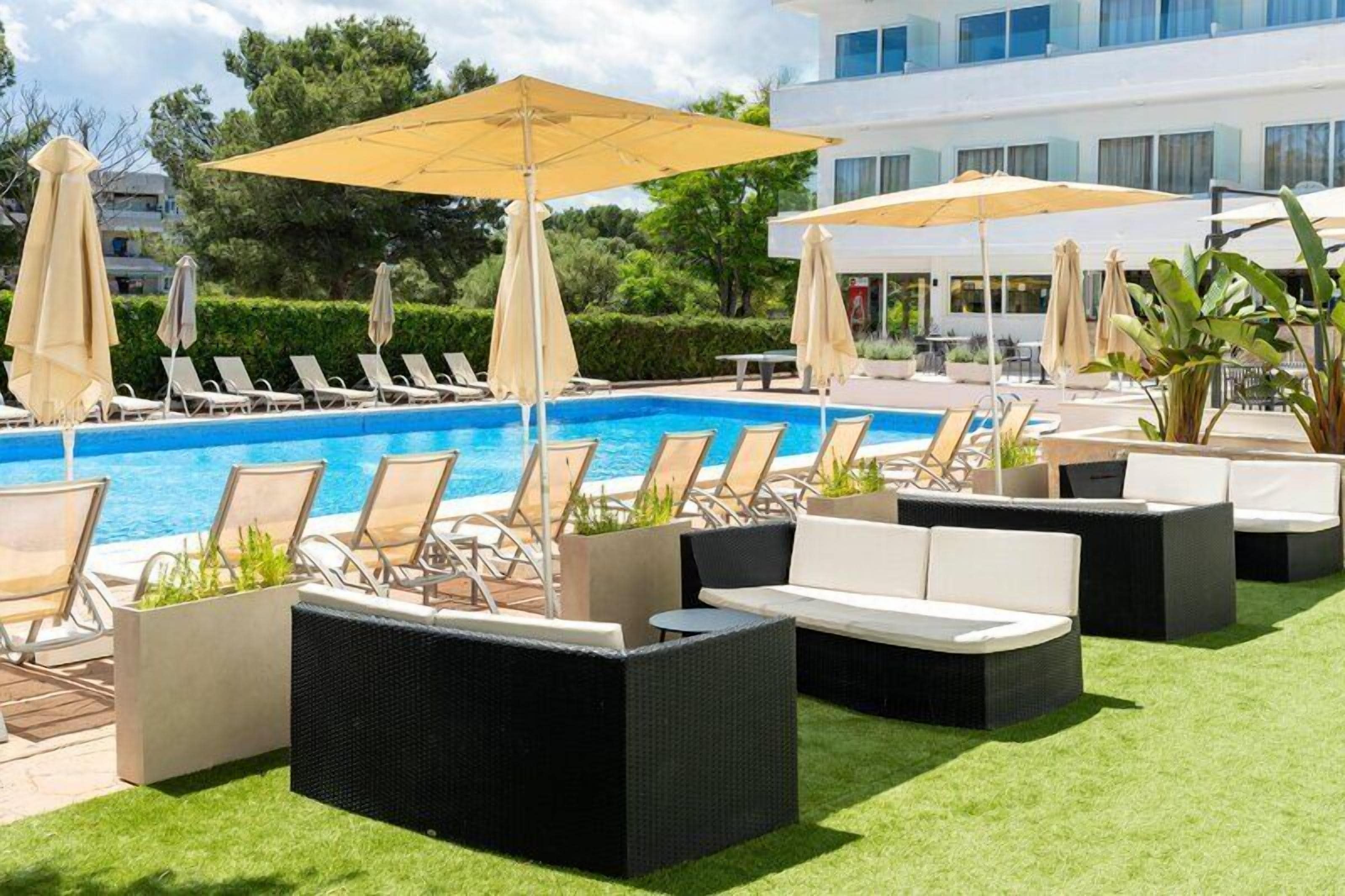 A poolside area with lounge chairs and umbrellas, a swimming pool, and a building in the background.