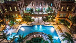 Un hôtel à plusieurs étages doté d’une piscine centrale, de palmiers et d’espaces de détente en plein air.