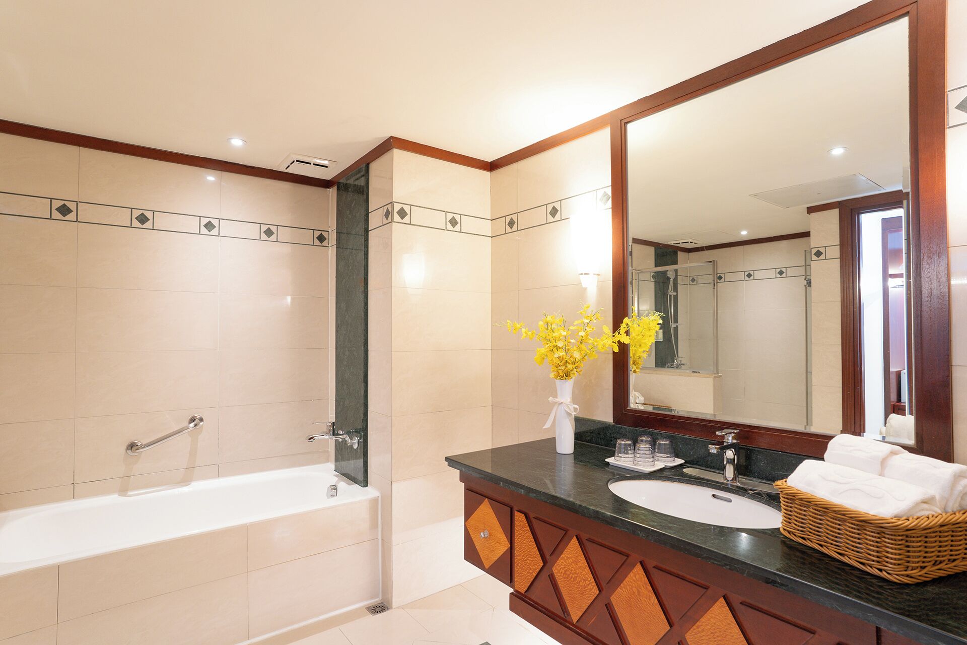 A modern bathroom with a bathtub, a sink, a large mirror, and a vase with yellow flowers.
