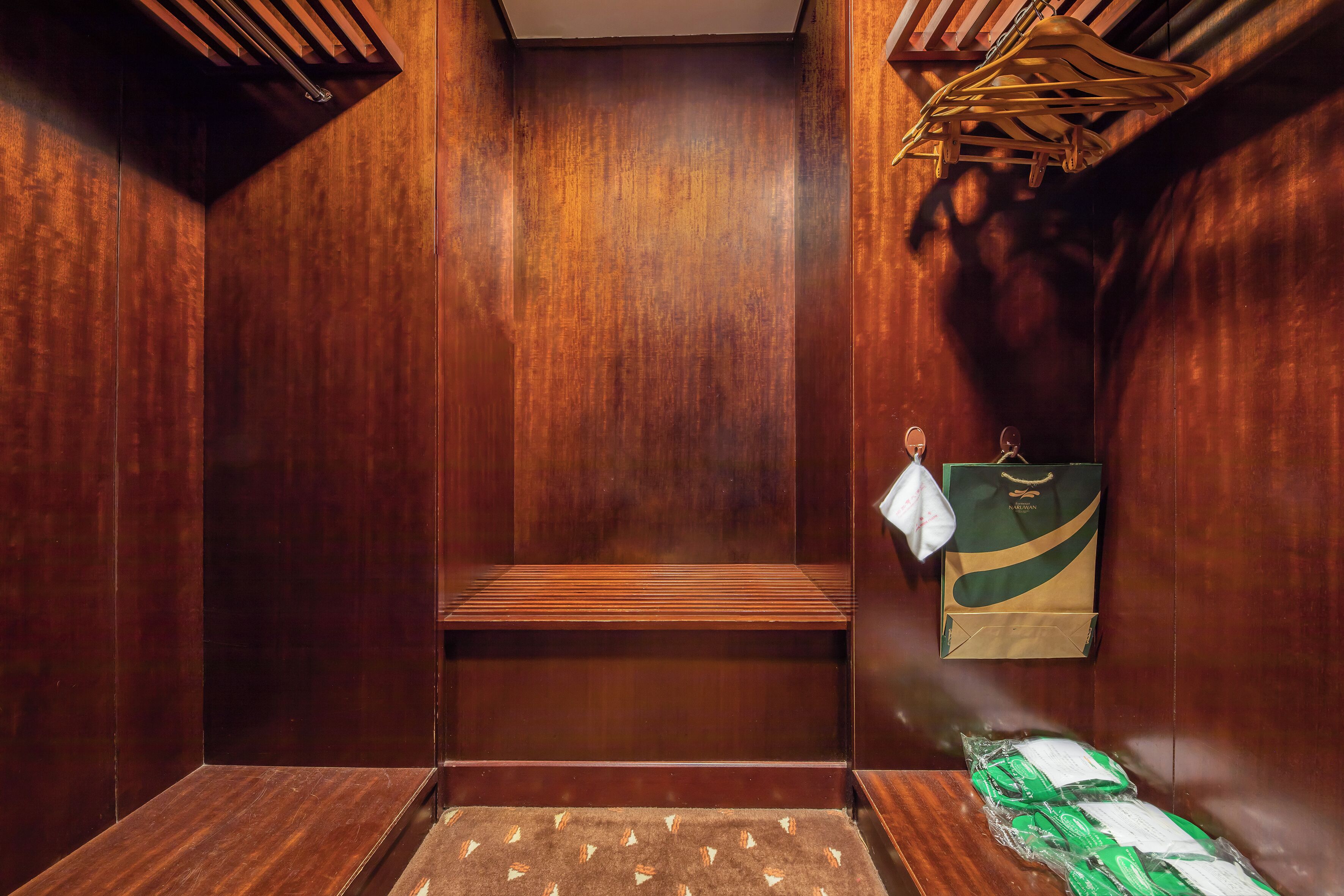 A wooden interior with a bench, a trash bin, and a hanging bag.
