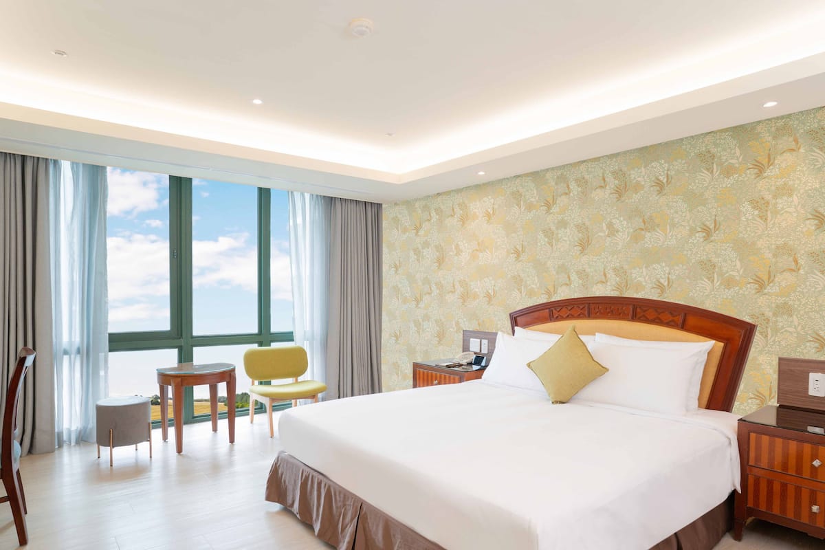 Habitació d'hotel amb un llit gran, un escriptori petit, una cadira i vista al cel per la finestra.
