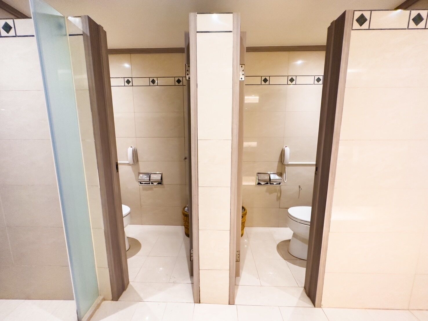 Un baño con espejo, dos inodoros, una ducha y un secador de manos.