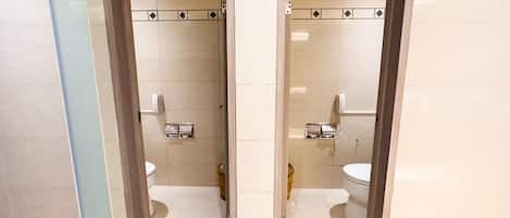 Un baño con espejo, dos inodoros, una ducha y un secador de manos.